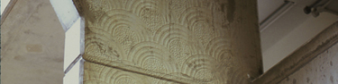 Strip taken from larger photograph showing scallop wall paper patterns projected on to a a large, flat concrete pillar.