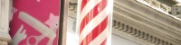 Photograph of a red and white barbers pole, next to a pink and white sign which features the outline of some scissors, a comb and a hand.